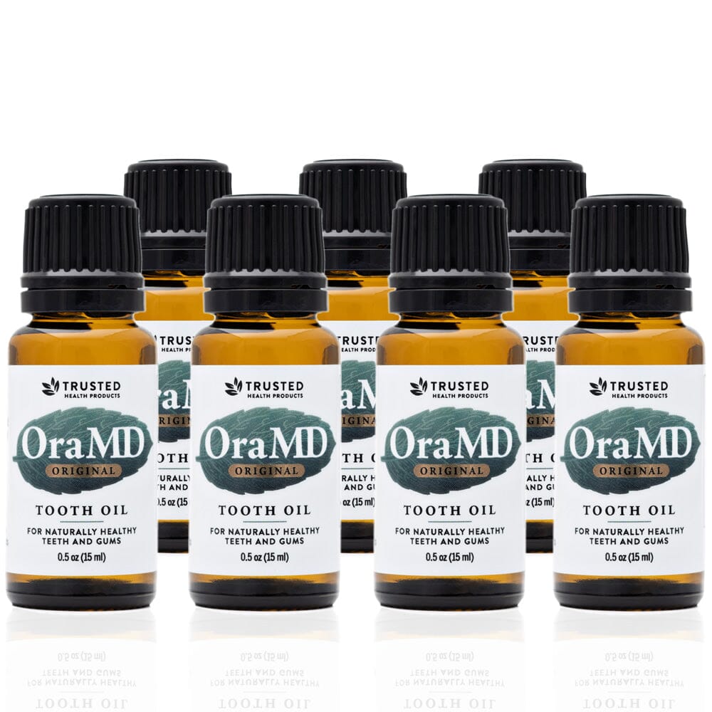 A set of seven Toothpaste Alternative OraMD tooth oil bottles in amber packaging with white and green labeling, indicating the product is a dental health aid.