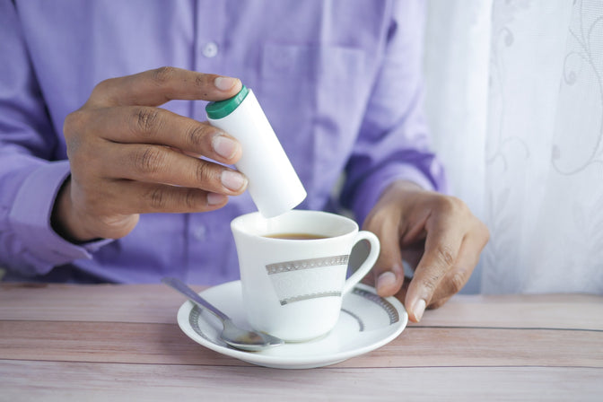 person adding sugar substitute to coffee