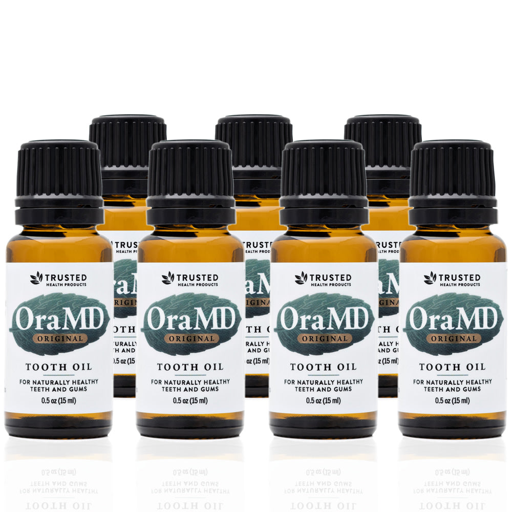 A set of seven Toothpaste Alternative  OraMD tooth oil bottles in amber packaging with white and green labeling, indicating the product is a dental health aid.