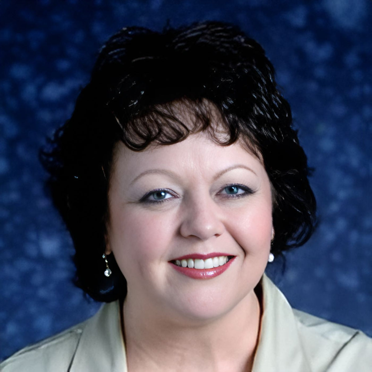 Woman with short dark hair smiling against a blue background